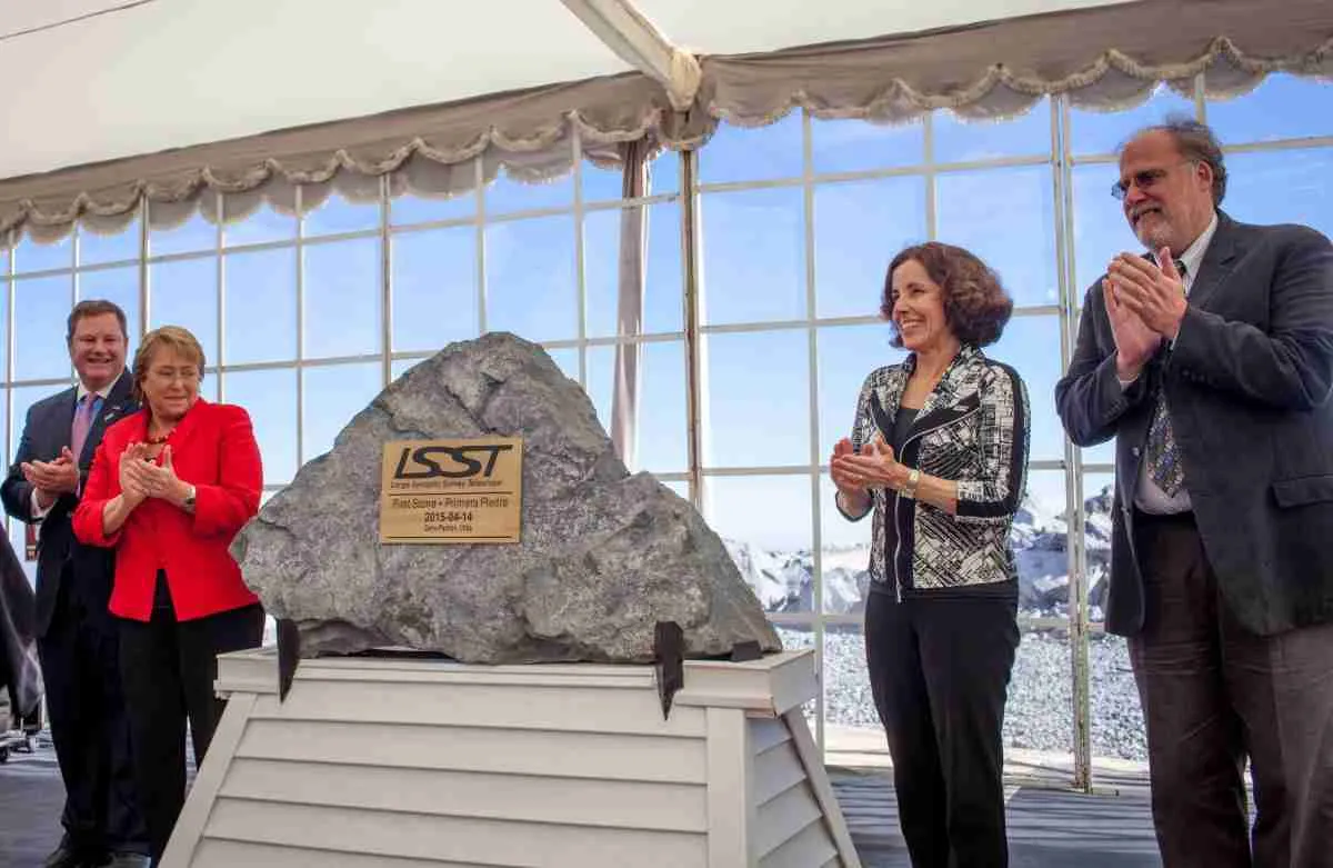 An image of four LSST Discovery Alliance leaders are gathered around a giant rock clapping their hands at the First Stone Event with snowy mountains in the background.