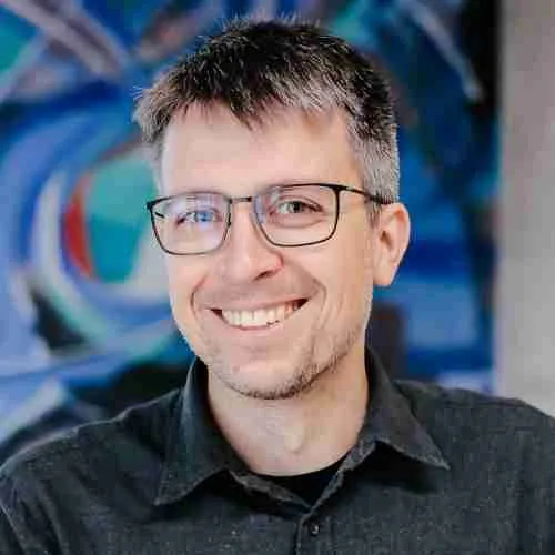 headshot of a man smiling with glasses